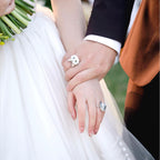 A close-up of a bride and groom holding hands, showcasing two distinct bespoke 3D pet portrait rings custom hand-sculpted as luxury wedding sentimental keepsakes.