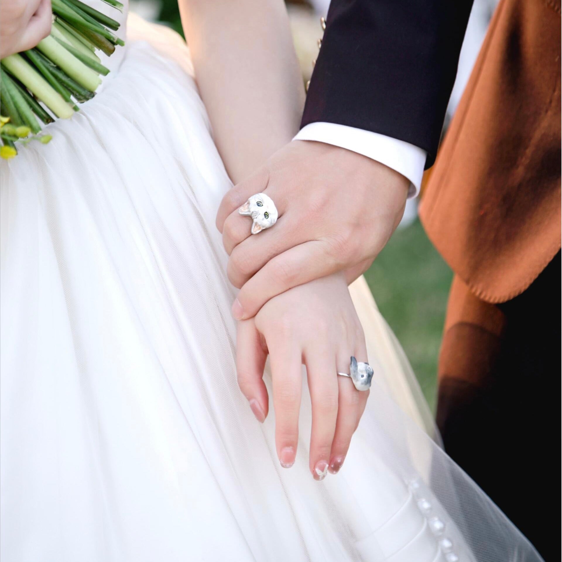 A close-up of a bride and groom holding hands, showcasing two distinct bespoke 3D pet portrait rings custom hand-sculpted as luxury wedding sentimental keepsakes.