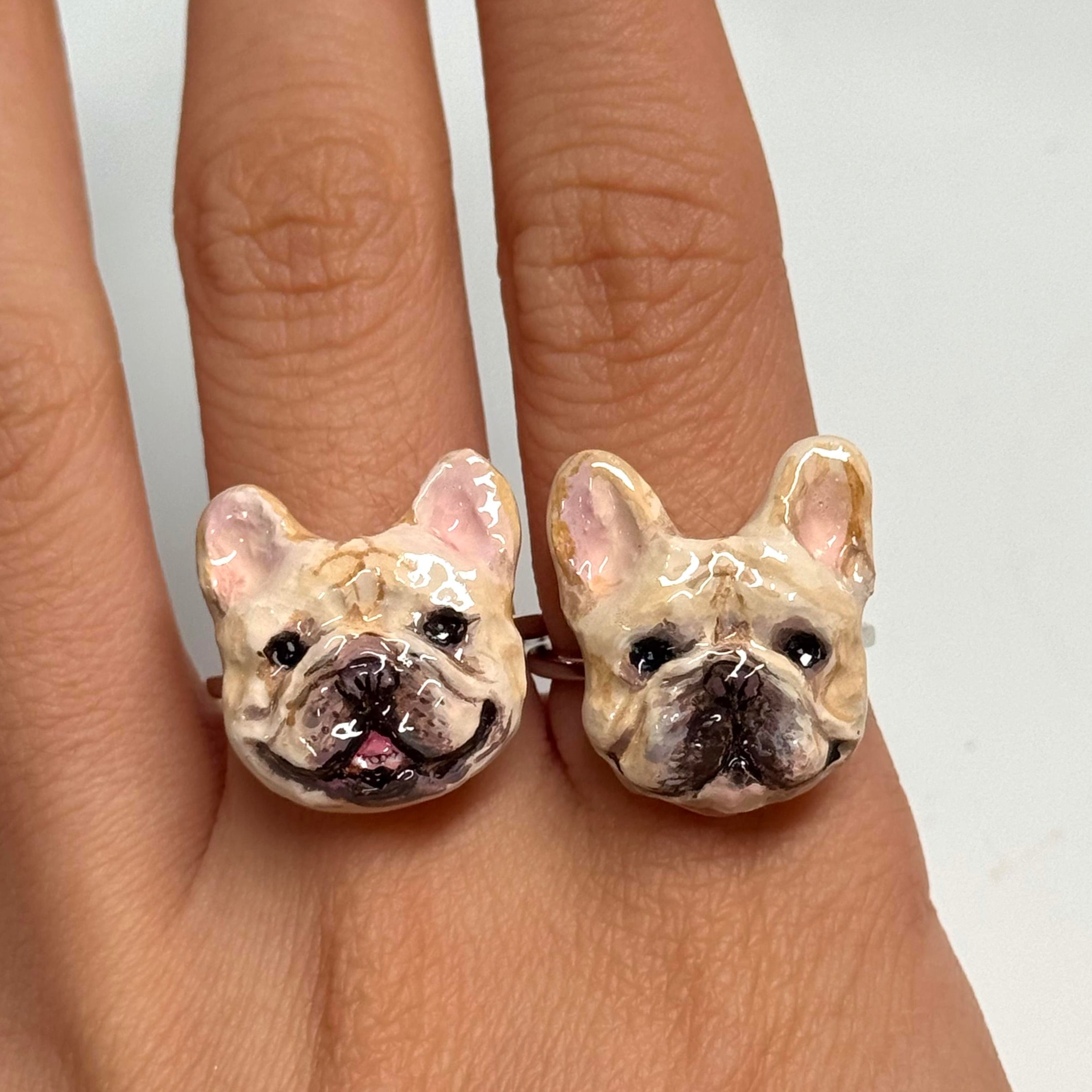 Two bespoke 3D French Bulldog portrait rings worn on fingers, custom hand-sculpted as a luxury wedding keepsake jewelry for Frenchie parents.