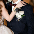 Person wearing a boutonniere with a small stuffed animal and flowers on a dark suit.