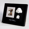 Black framed photo with a small white sculpture and tag on a light gray background