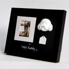 Black framed photo with a small white sculpture and tag on a light gray background