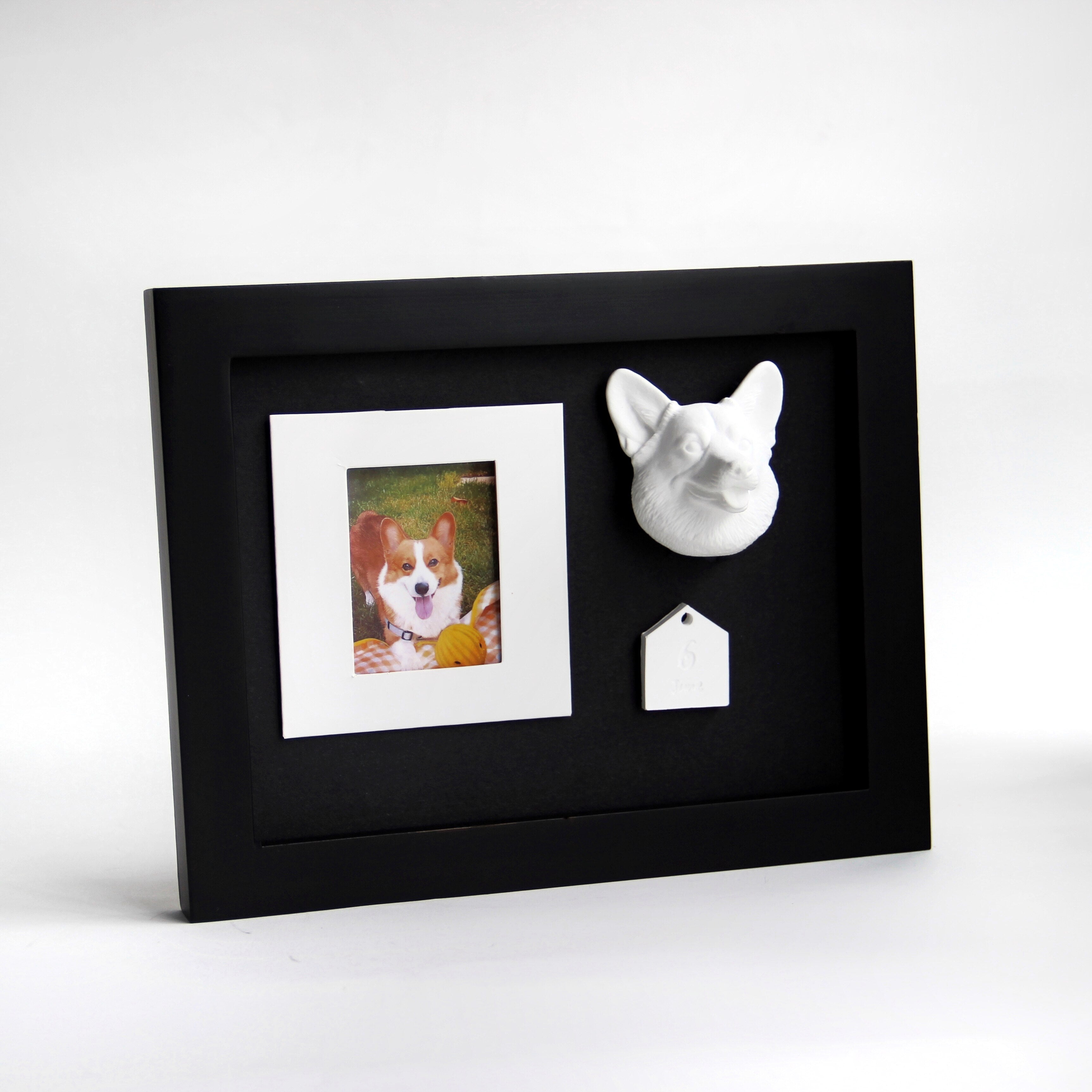 Black framed picture with a dog photo, dog figurine, and tag on a white background