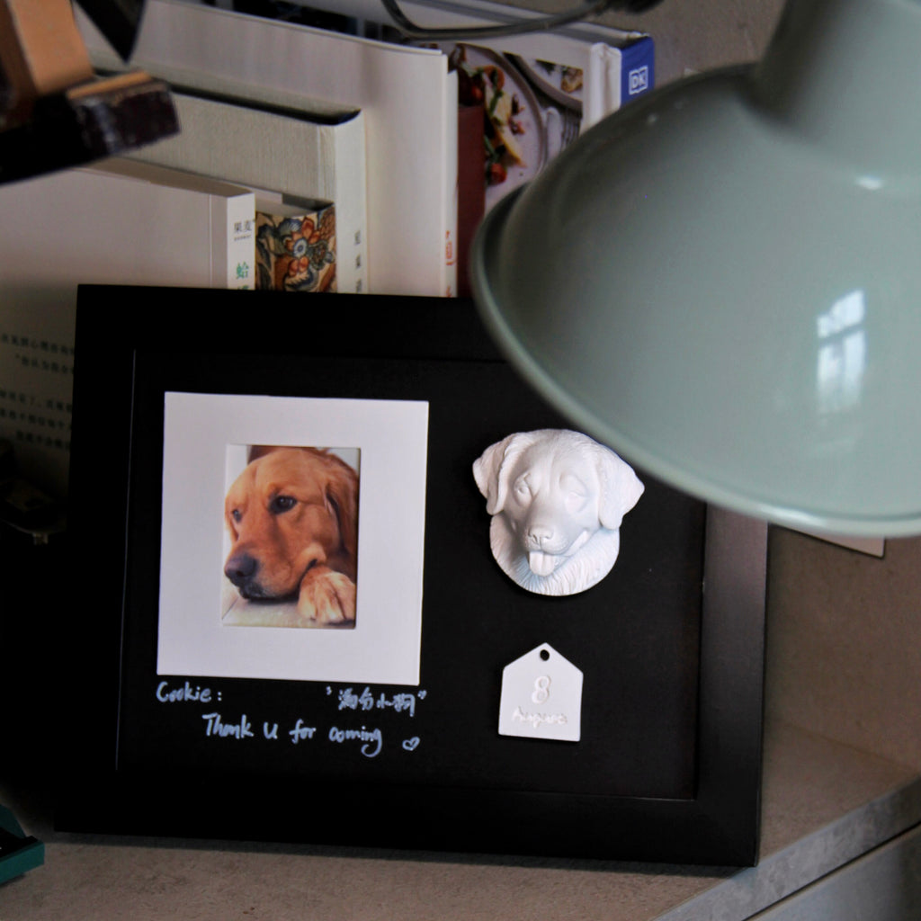 Black frame with a photo of a dog and a small white dog figurine on a surface.