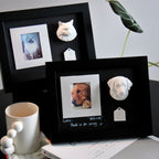 Black photo frames with pet portraits and 3D clay models on a desk.