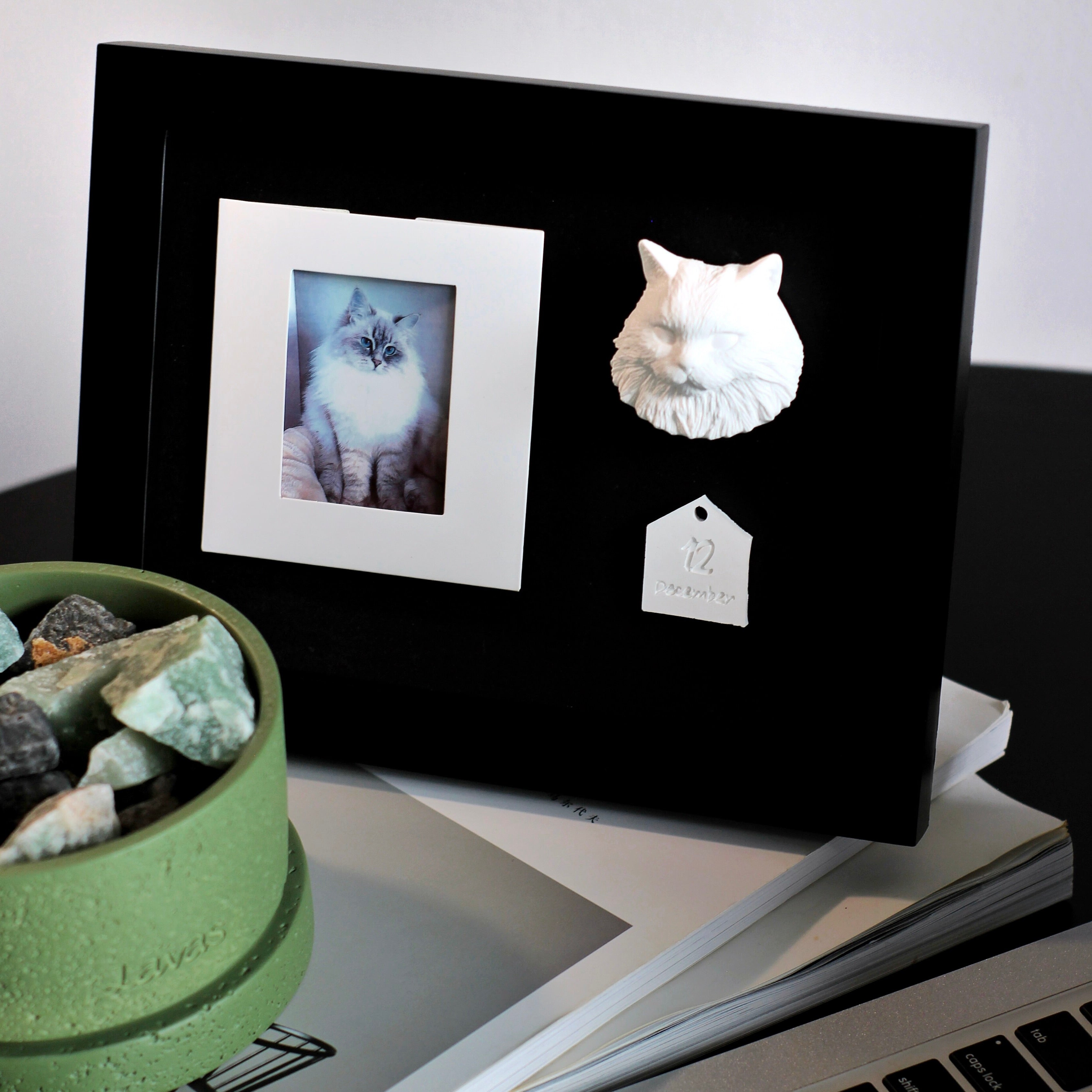 Black photo frame with a white cat sculpture and a small photo of a cat on a desk.