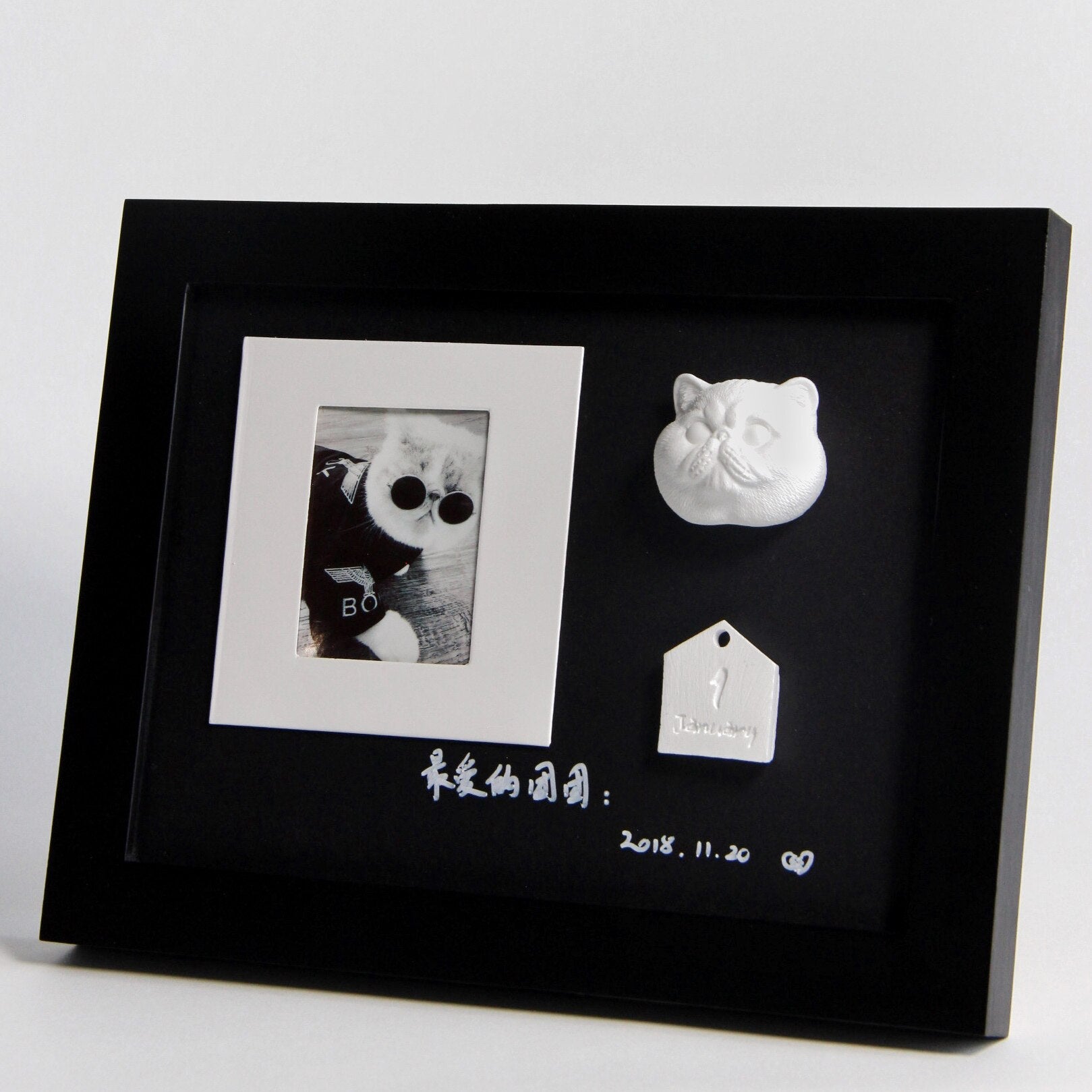 Black framed photo with a black and white photo, two small white sculptures, and text on a light gray background