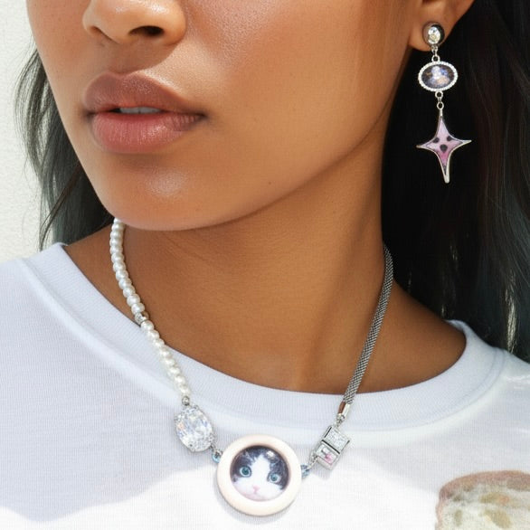 Close-up of a person wearing a necklace with a cat pendant and matching earrings.