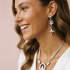 Woman wearing elegant earrings and a necklace with a pink pendant against a soft pink background