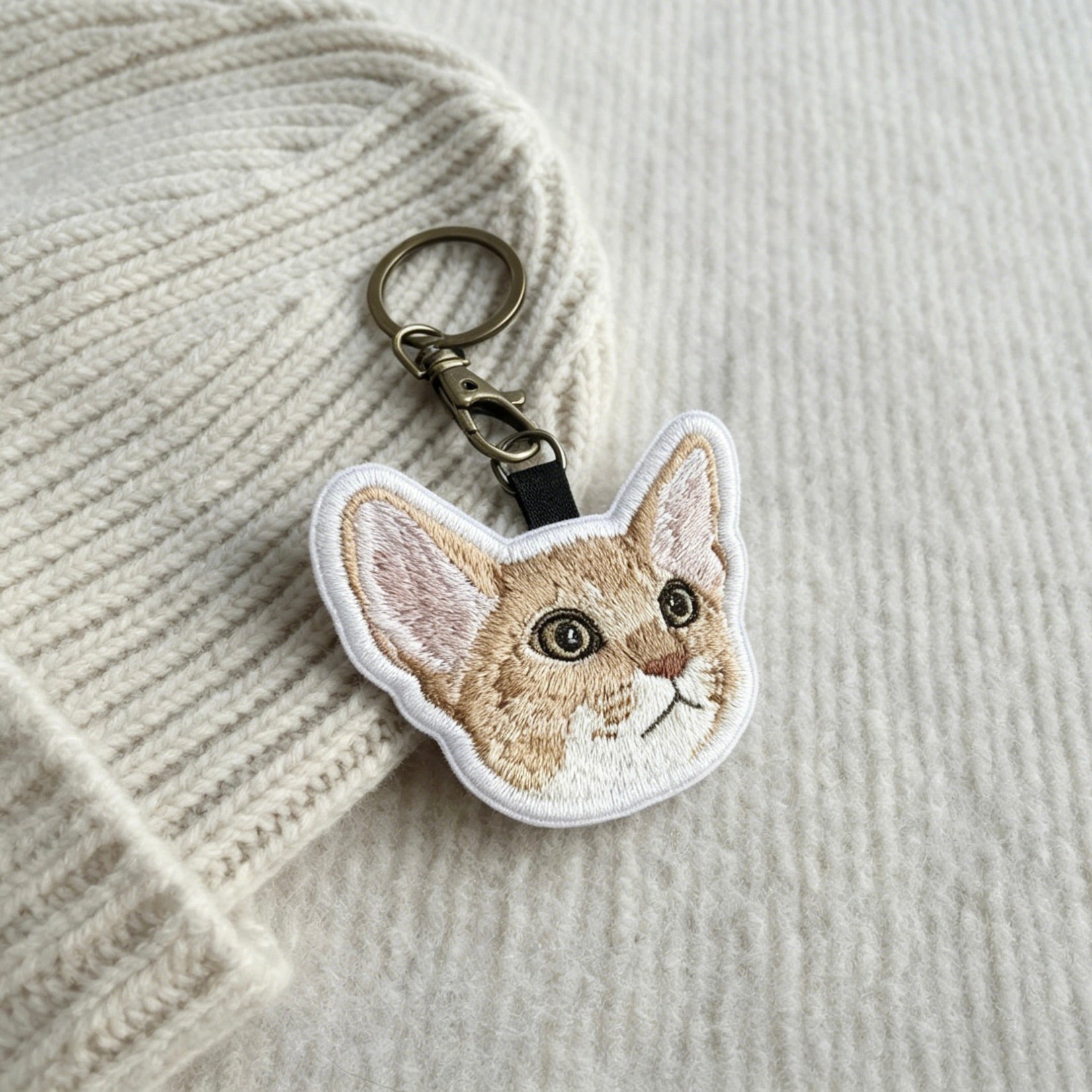 Embroidered cat keychain on a textured fabric background