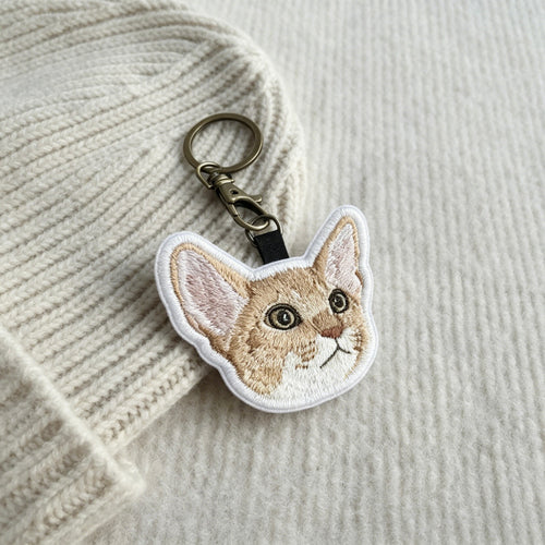 Embroidered cat keychain on a textured fabric background