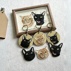 Set of cat-themed keychains in front of a framed picture of cats on a textured white surface.