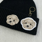 Black knit beanie with embroidered dog faces and a matching keychain on a light gray background.