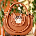 Brown handbag with a cat face design on a blurred natural background