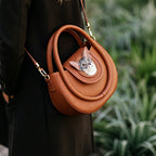Brown handbag with a cat-shaped handle held by a person in a blurred outdoor setting