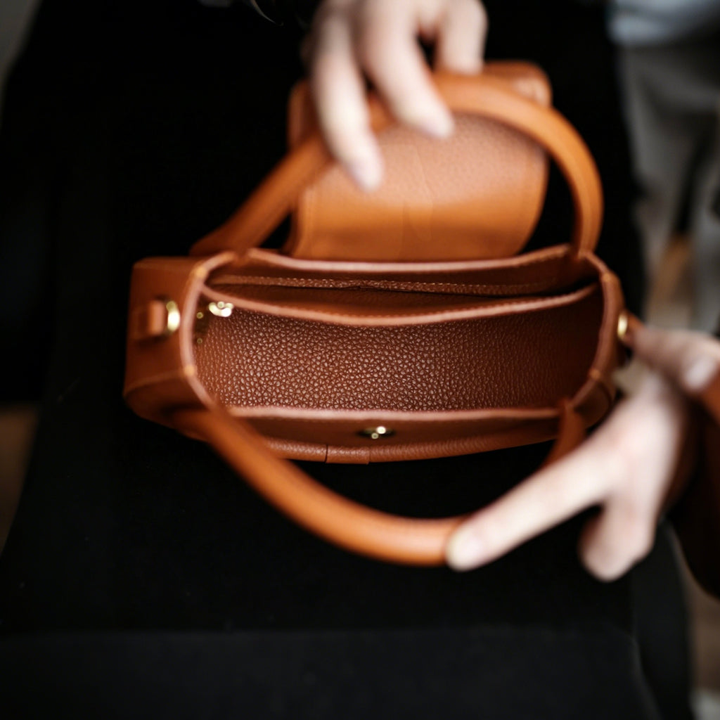 Brown leather handbag held by a person wearing white gloves