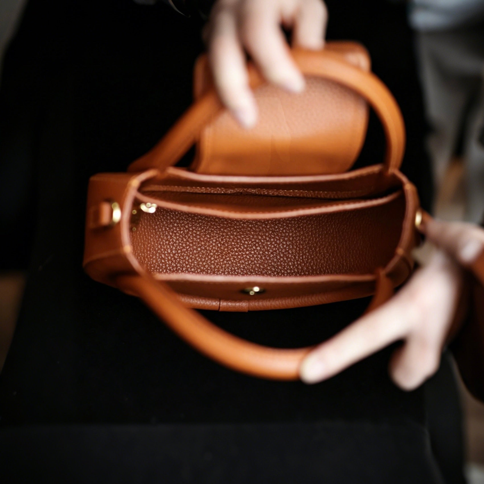 Brown leather handbag held by a person wearing white gloves