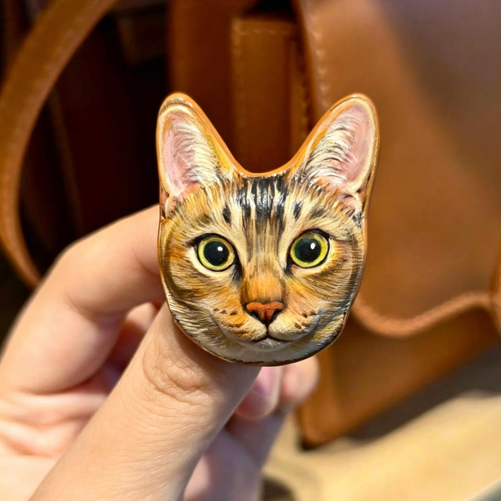 Hand holding a wooden ornament with a cat's face design against a brown background