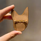 Gold cat-shaped brooch held between fingers against a neutral background