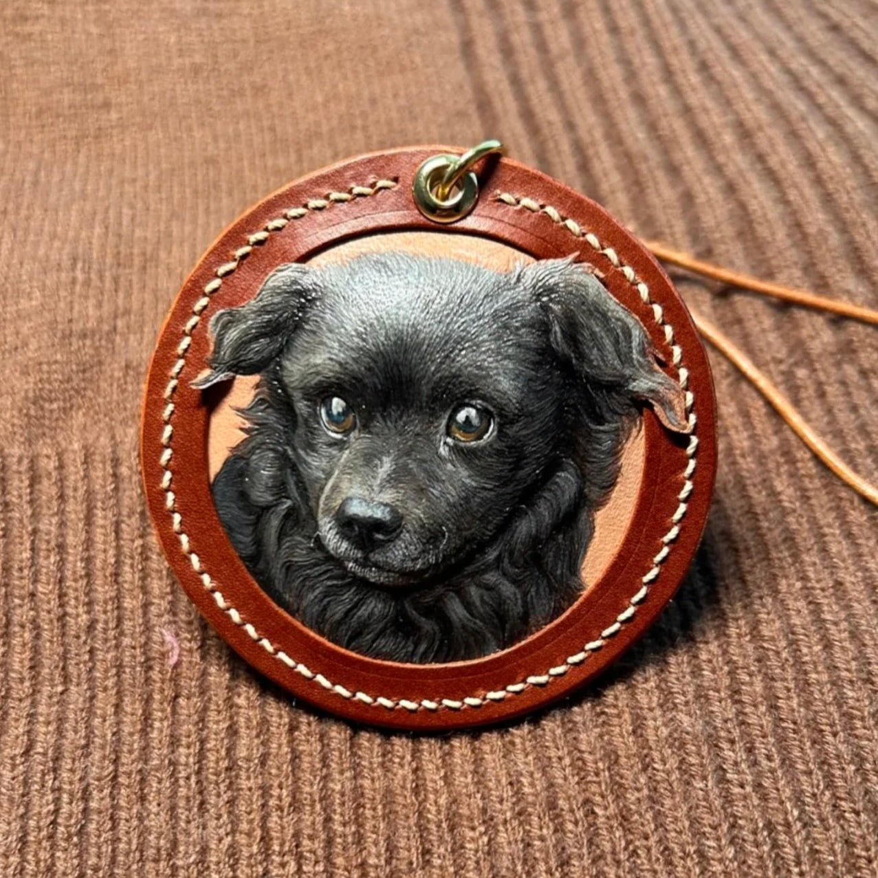 Round leather pendant with a black puppy's face on a brown textured background