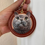 Keychain with a cat's face design held by a hand against a white background