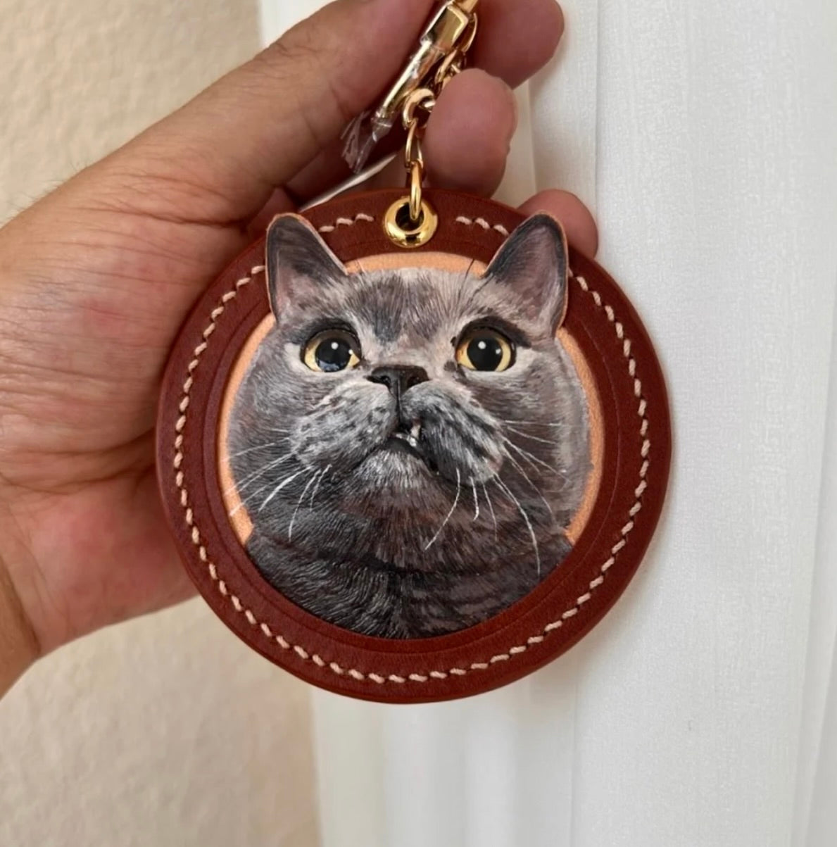 Keychain with a cat's face design held by a hand against a white background