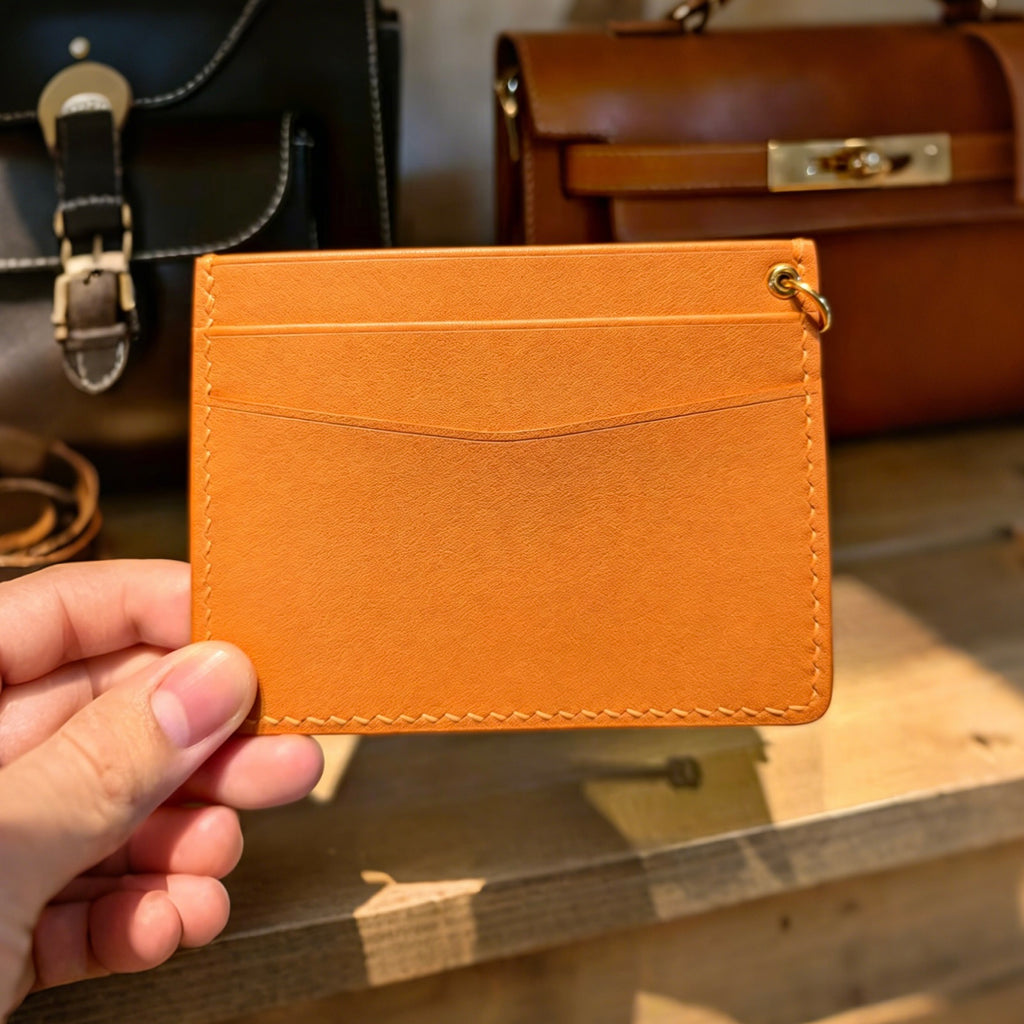 Hand holding a brown leather cardholder with bags in the background