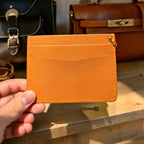 Hand holding a brown leather cardholder with bags in the background