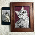 Framed portrait of a cat next to a smartphone displaying a similar image on a textured white background