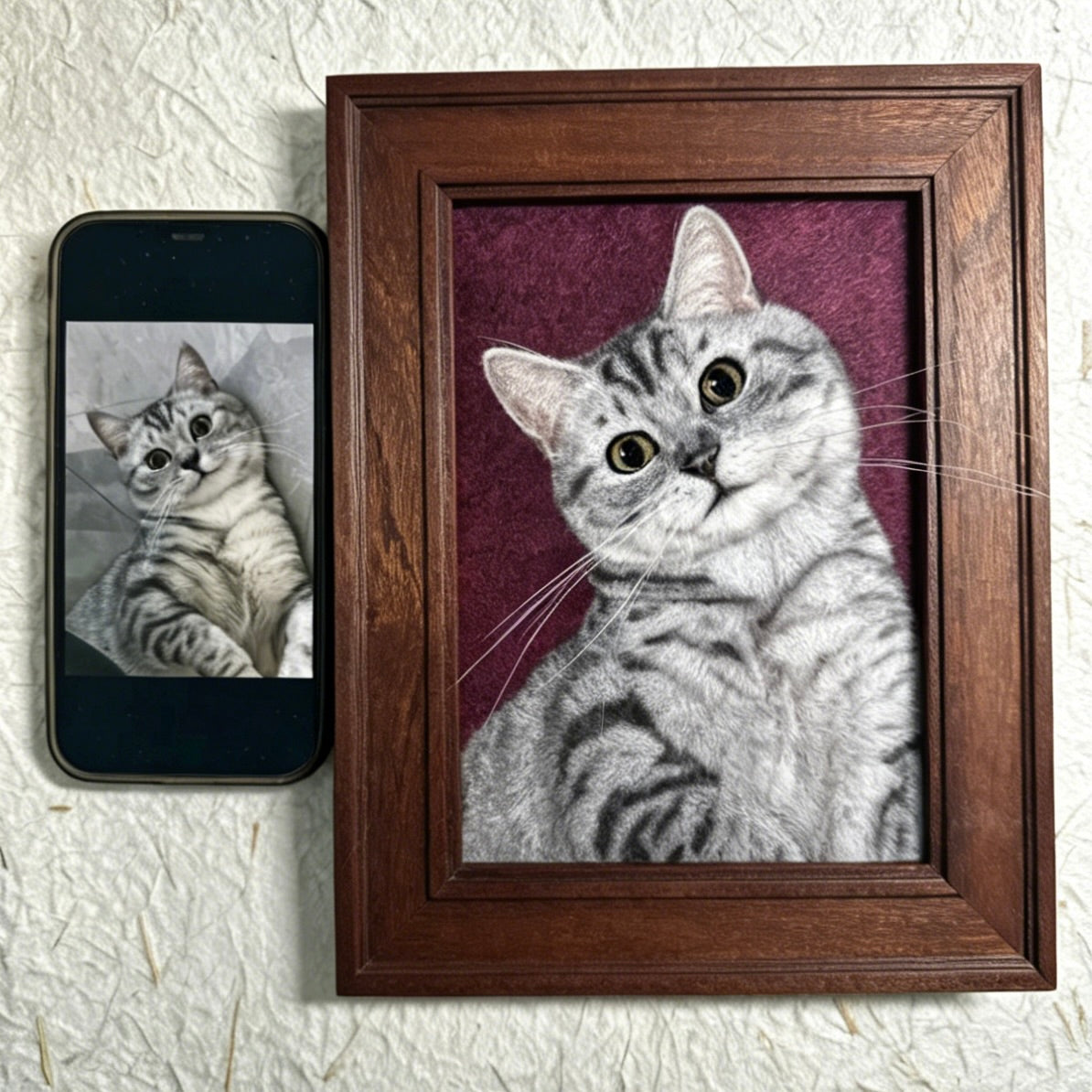 Framed portrait of a cat next to a smartphone displaying a similar image on a textured white background