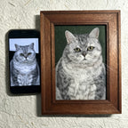 Framed portrait of a cat next to a smartphone displaying the same image on a textured wall.
