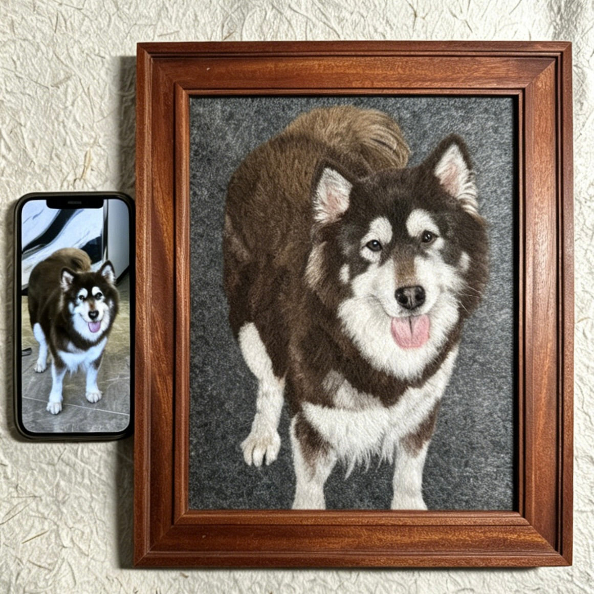Framed needlepoint of a dog next to a smartphone with a photo of the same dog.