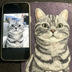 Realistic drawing of a cat next to a smartphone displaying a photo of a cat.