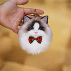 Cat-shaped keychain with a red bow tie held by a hand against a blurred background