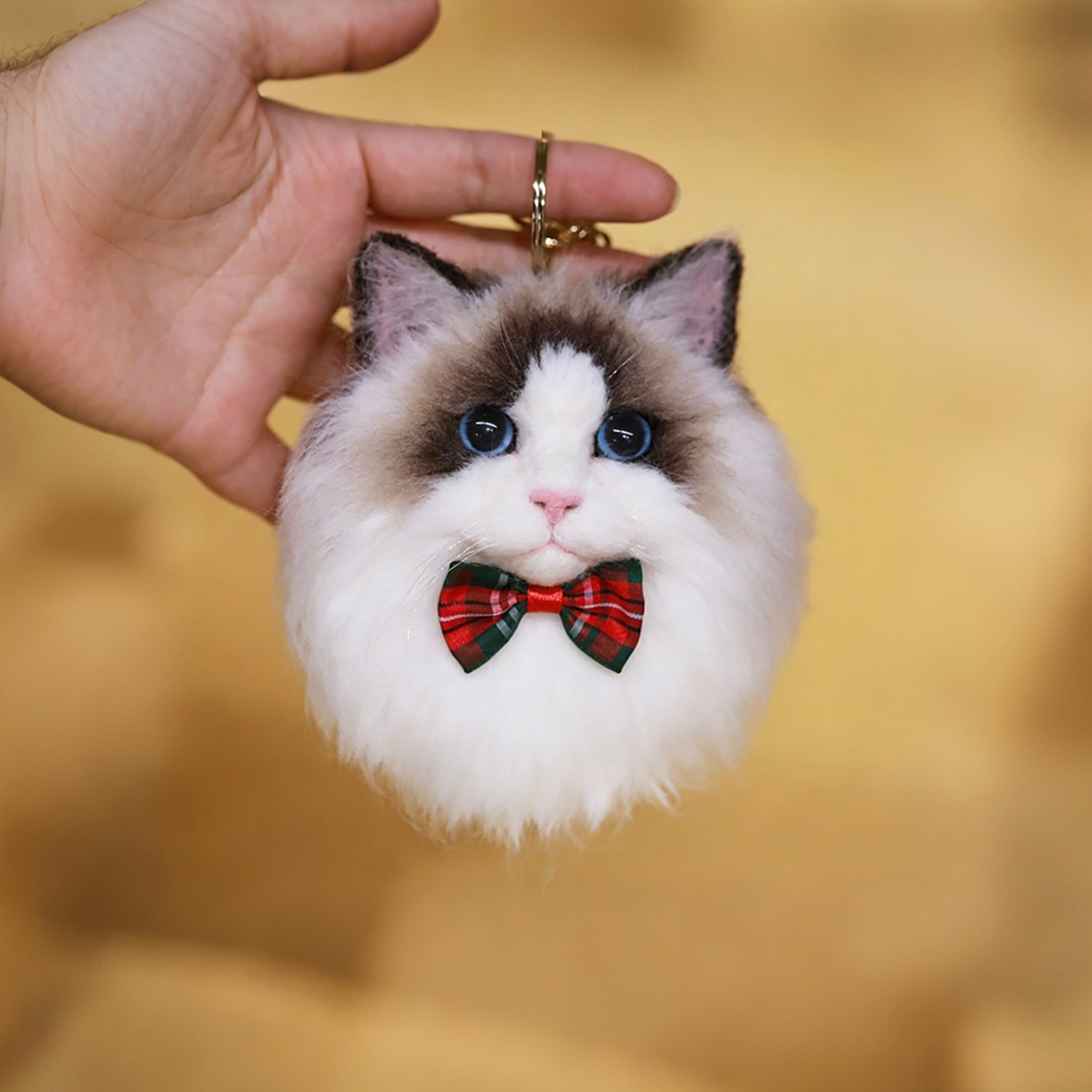 Cat-shaped keychain with a red bow tie held by a hand against a blurred background