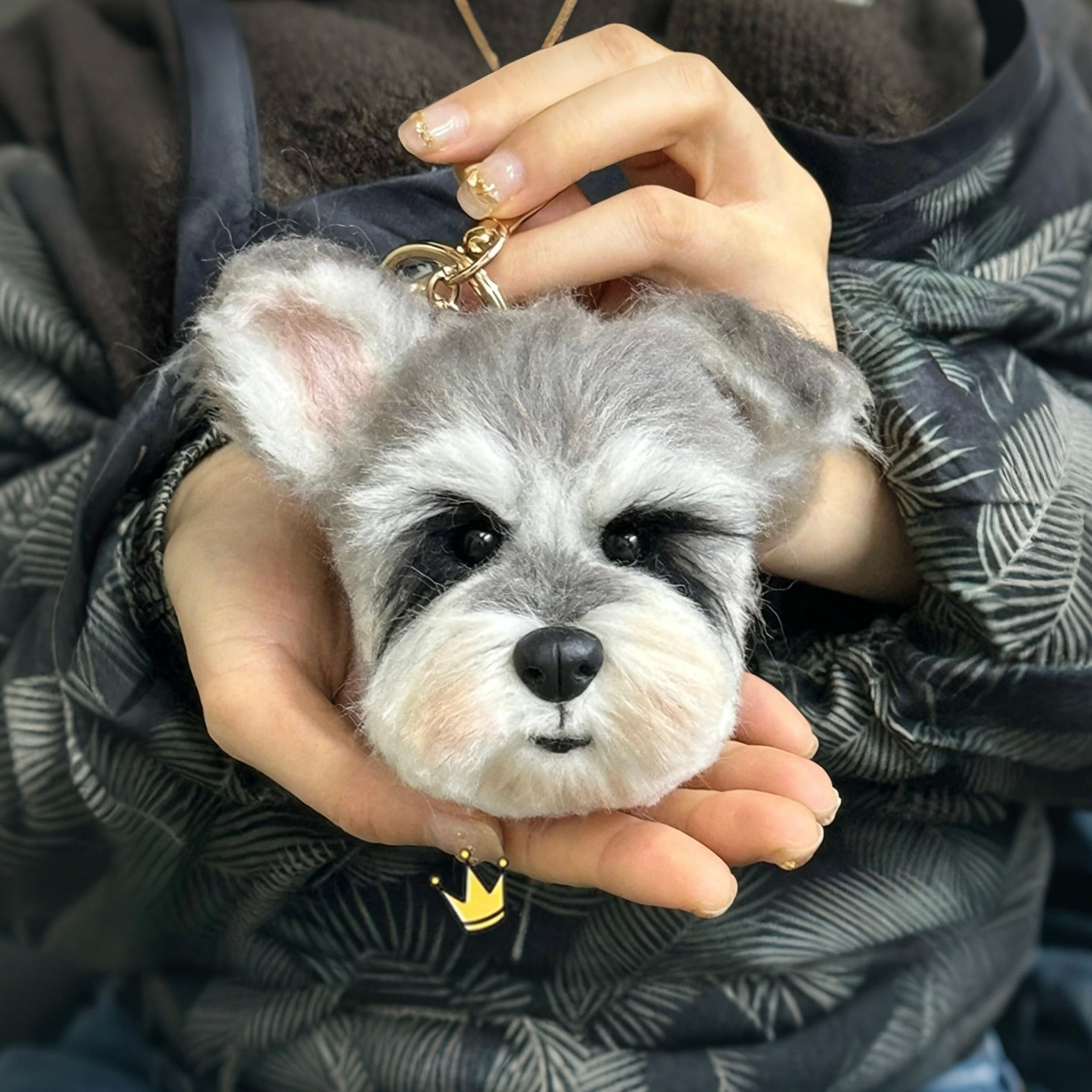 Person holding a small dog-shaped keychain with a patterned scarf in the background