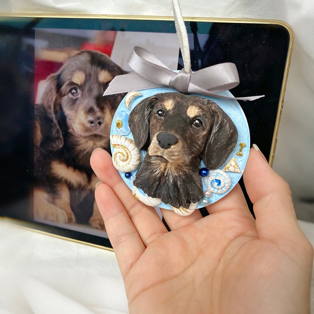Decorative ornament with a dog's face on it held by a hand, with a framed picture of a dog in the background.