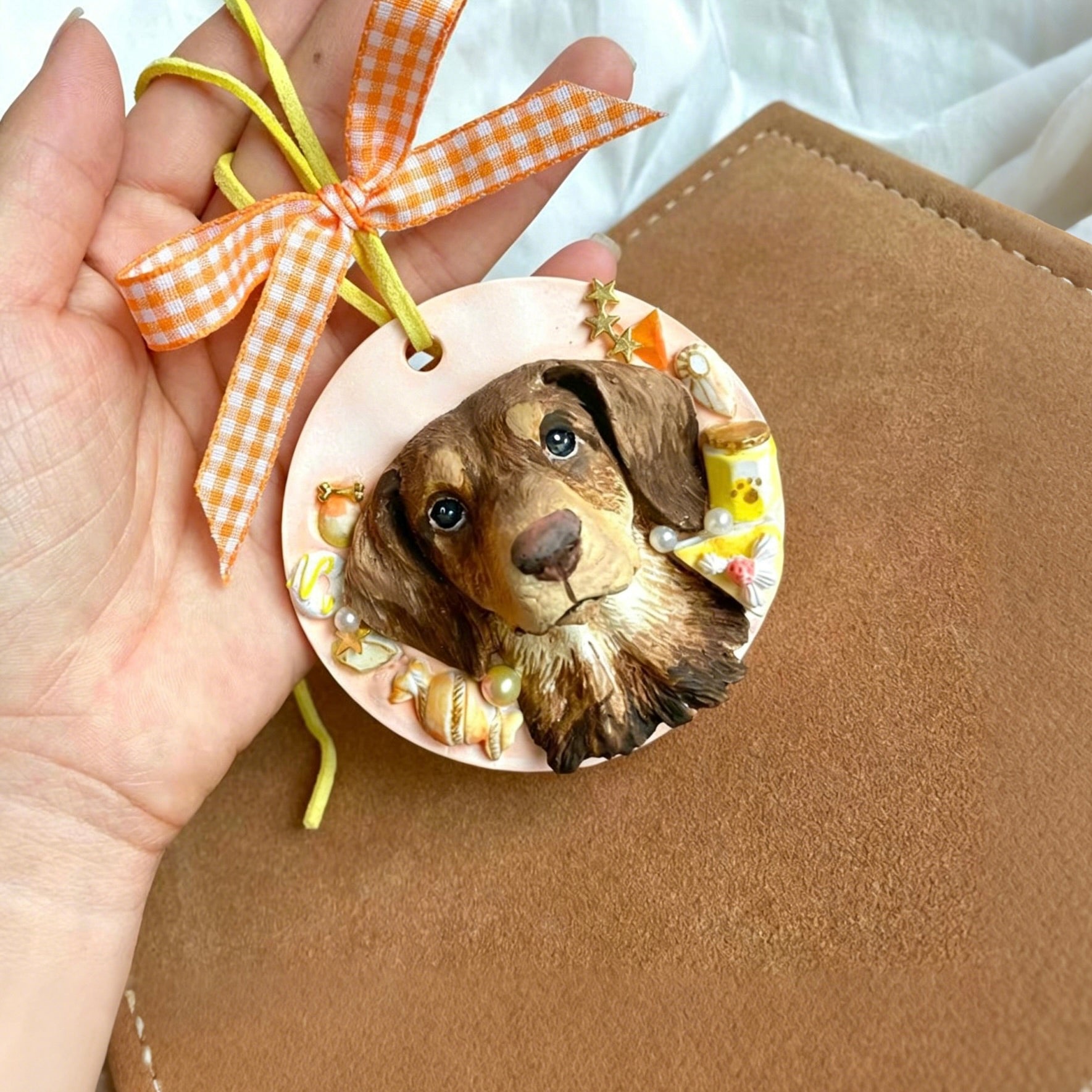 Round ornament with a dog's face on a hand holding it against a brown surface.