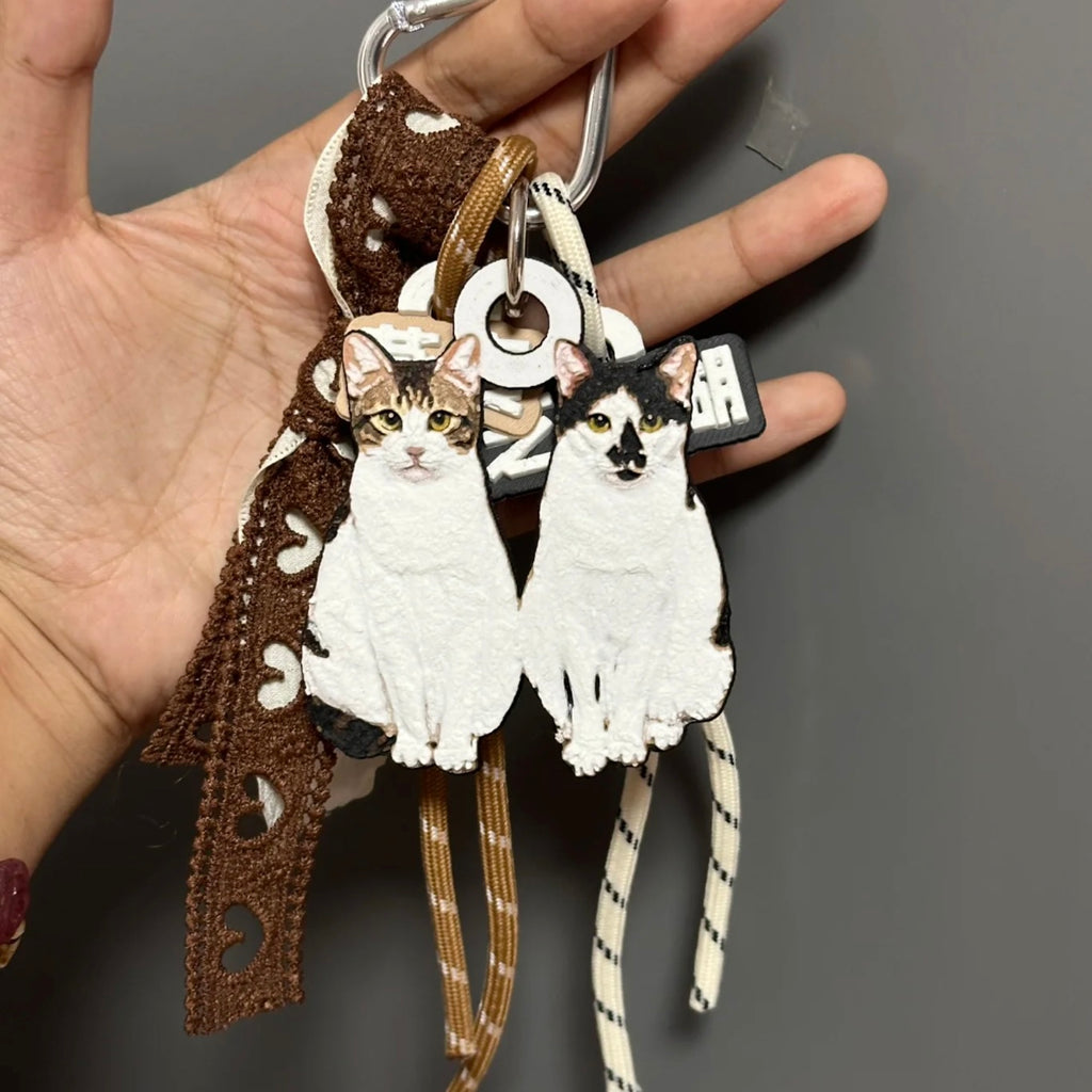 Cat-shaped keychains with a decorative ribbon held by a hand against a gray background