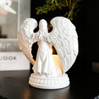 White angel figurine with wings holding a candle on a dark surface.