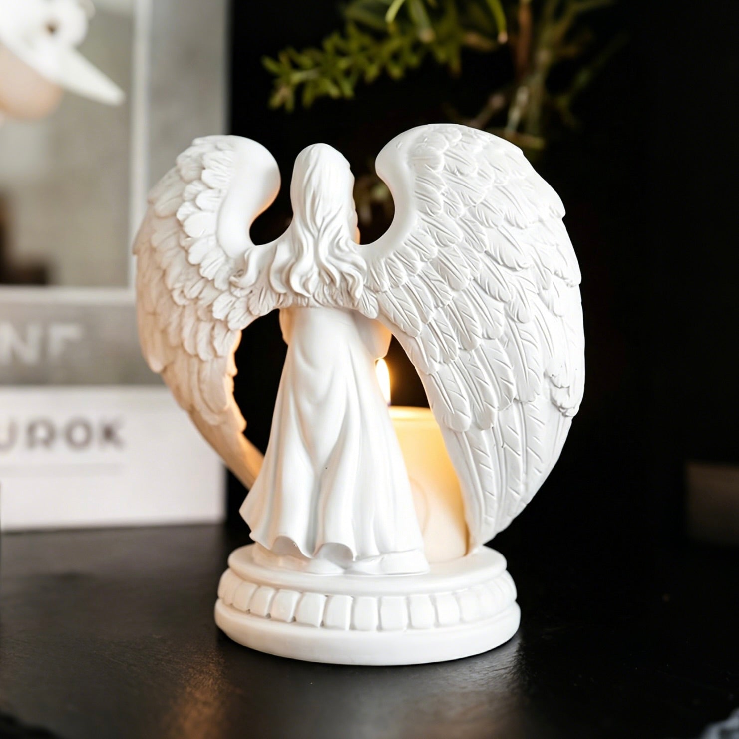White angel figurine with wings holding a candle on a dark surface.