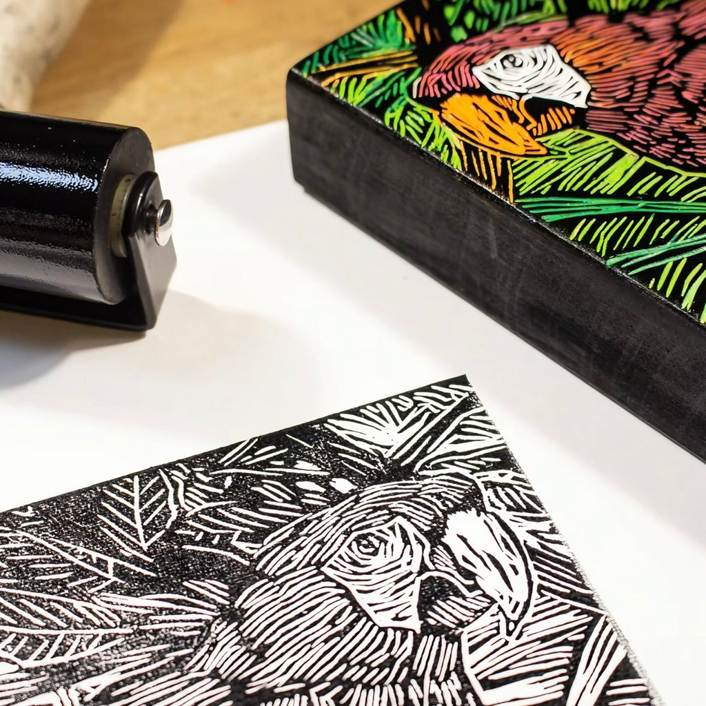 Linocut block with a printed design of a rooster and a roller on a white surface.