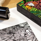 Linocut block with a printed design of a rooster and a roller on a white surface.