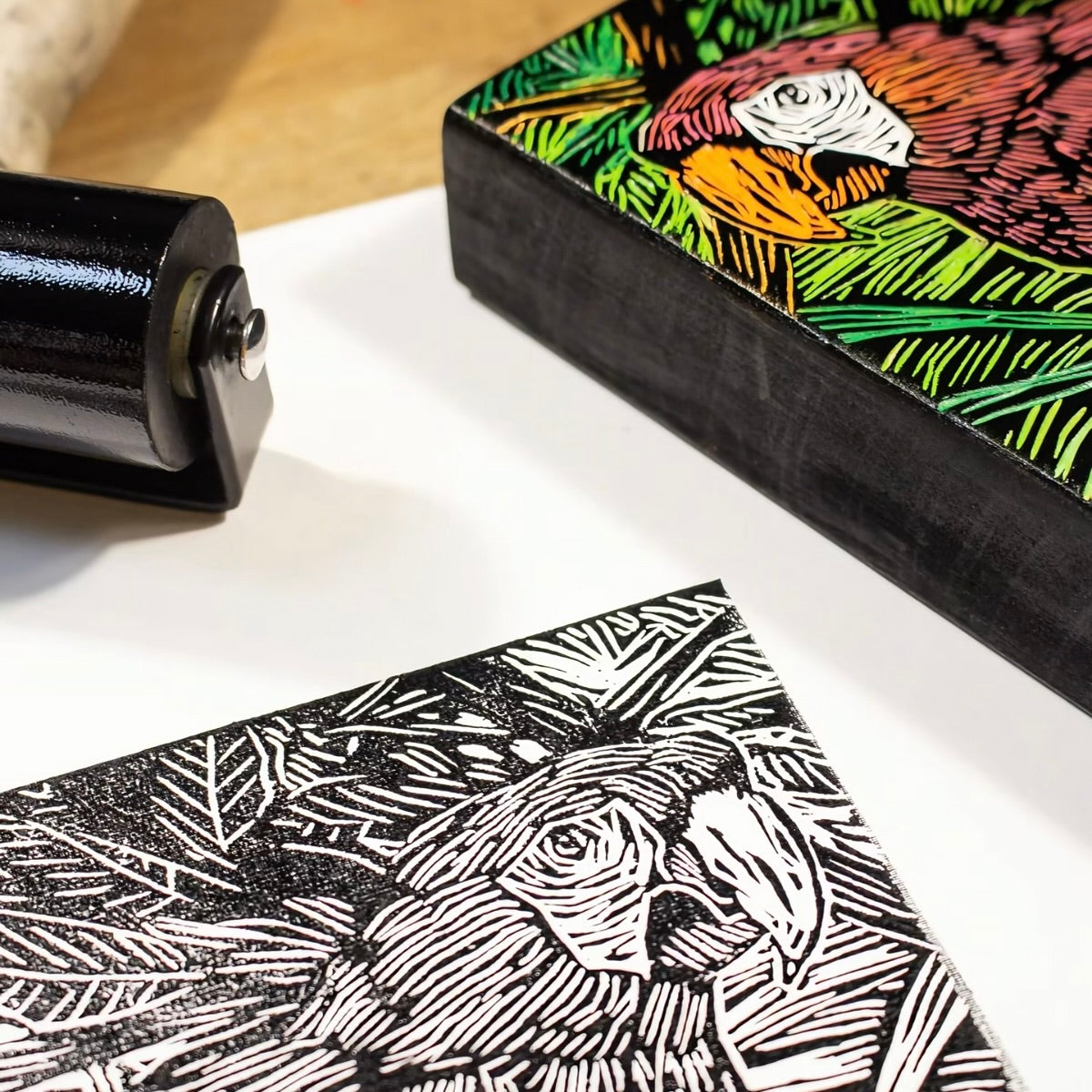 Linocut block with a printed design of a rooster and a roller on a white surface.