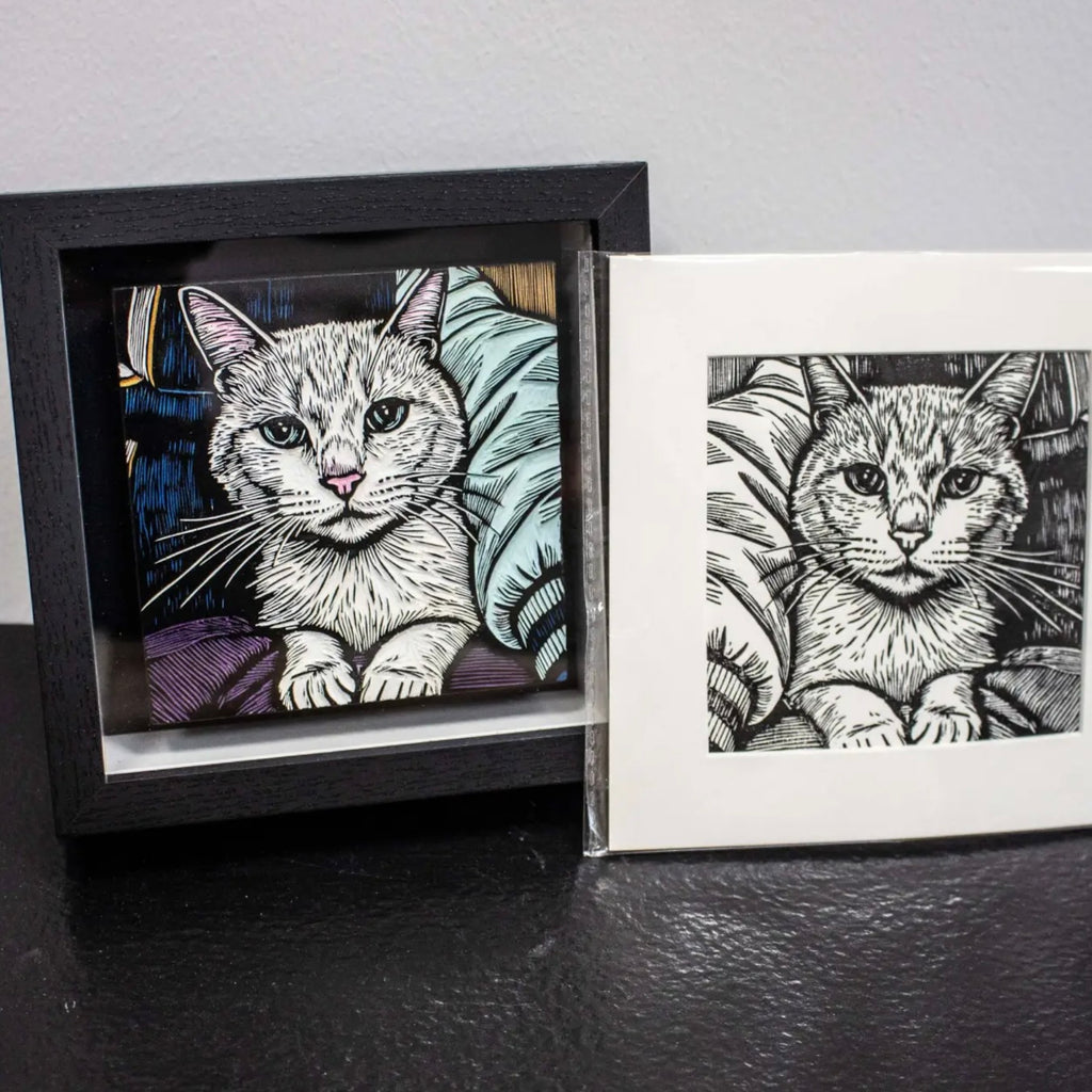 Two framed illustrations of cats on a dark surface with a light gray background
