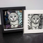Two framed illustrations of cats on a dark surface with a light gray background