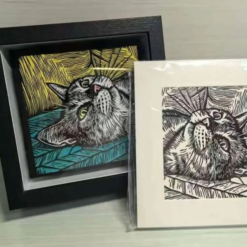 Framed and unframed cat illustrations on a gray surface