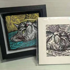 Framed and unframed cat illustrations on a gray surface