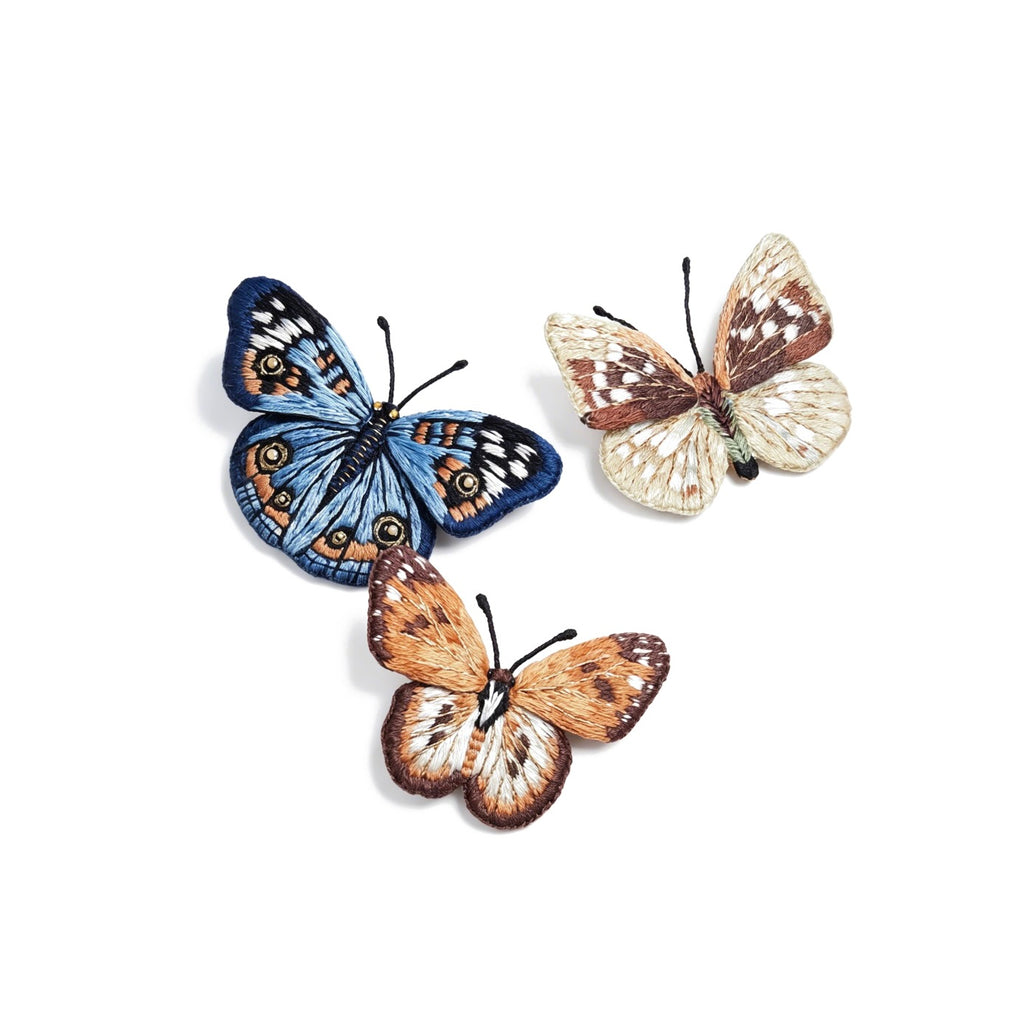 Three realistic hand-embroidered butterfly brooches: one blue butterfly and two in natural brown tones, showcased on a neutral background.