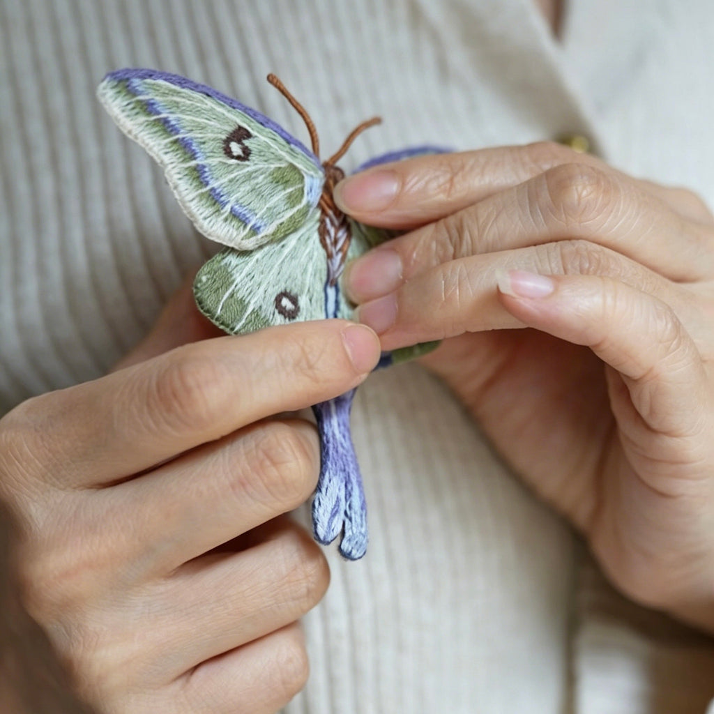A model's hand holds a realistic custom hand-embroidered butterfly brooch pin to display its wearable size and delicate finish.